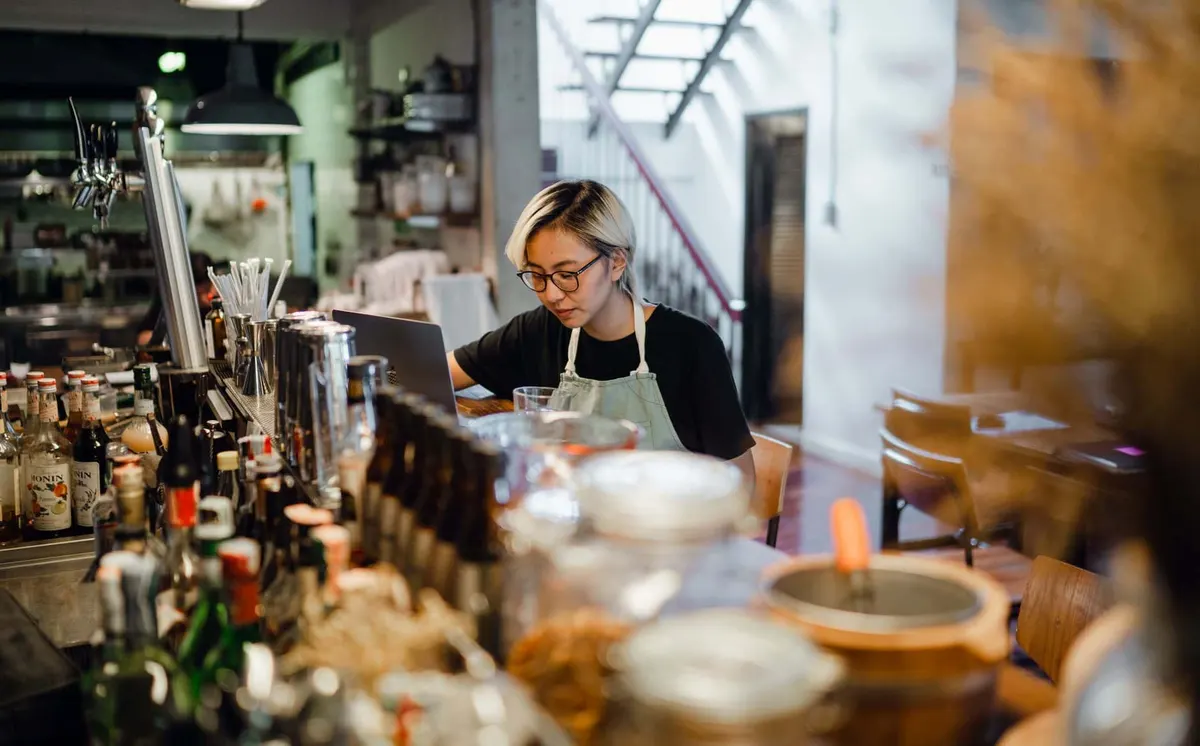 Restauratrice au comptoir de son établissement travaillant sur un ordinateur portable